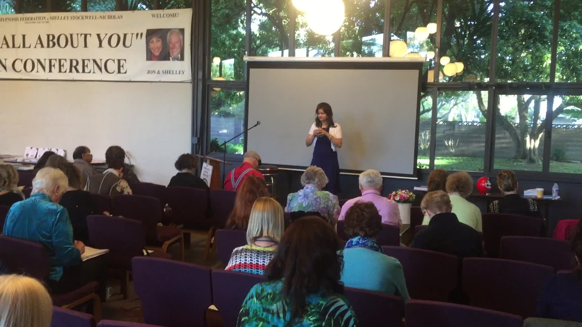 Hena speaking at a conference with a seated audience
